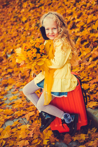 金发小女孩和手提箱在秋季背景