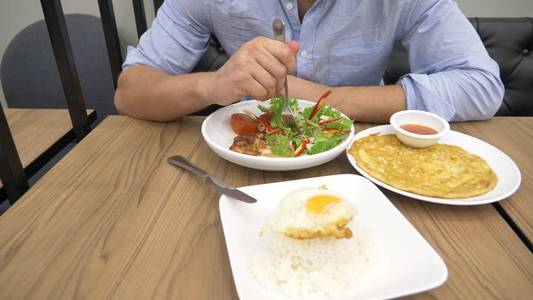 泰国菜米饭, 煎蛋卷, 蔬菜猪肉。一个人在餐馆里吃泰国菜