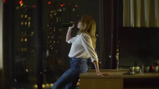 一个女人正在家里喝啤酒, 旁边是俯瞰摩天大楼的全景窗。夜晚, 背景模糊
