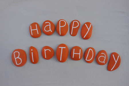 独特的生日快乐文本，由橙色的海石在白色的沙子上组成
