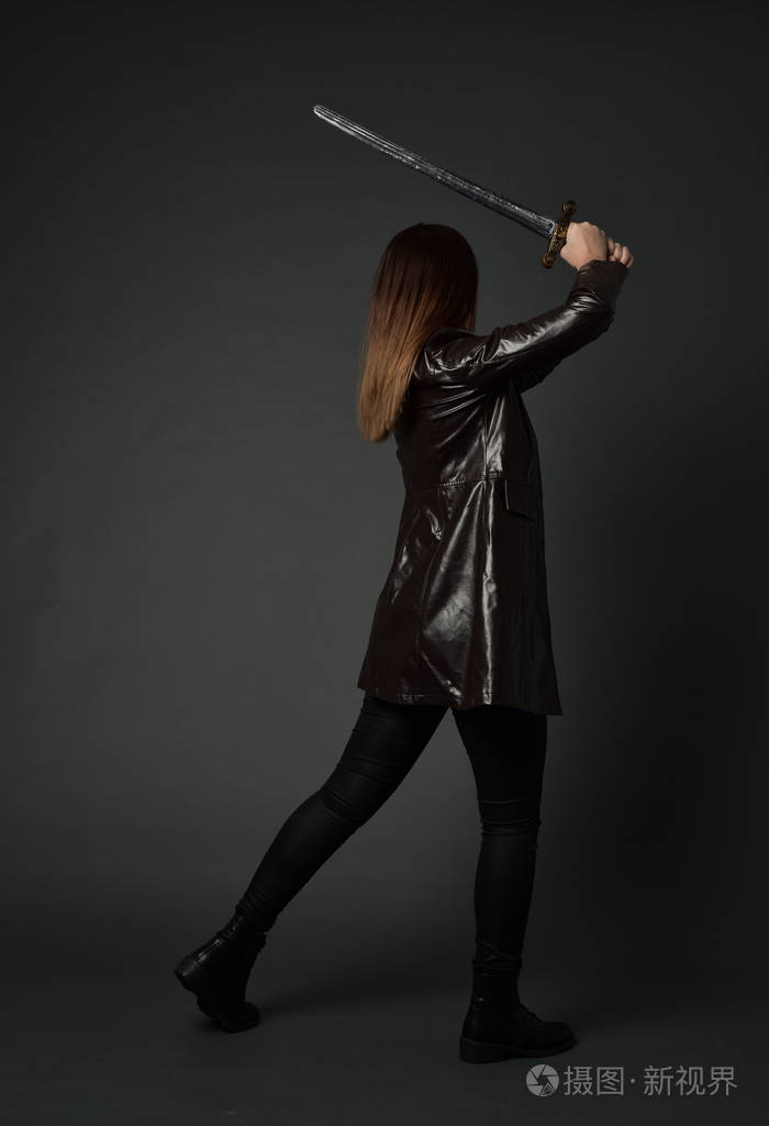 穿红色长皮杰克的黑发女孩的全长肖像站立姿势手持剑在灰色工作室背景