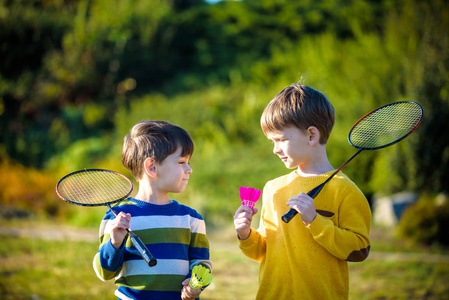 两个活跃的学龄前男孩在户外球场打羽毛球. 孩子们打网球.
