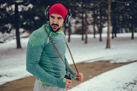 严肃的运动员在下雪的冬日里，一边听音乐一边从跳绳中休息