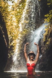 年轻的妇女旅游与草帽和红色泳装在深丛林与瀑布。真正的冒险概念。巴厘岛