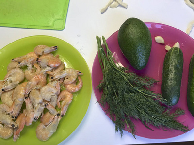 膨松糕点，牛油果黄瓜和厨房用具躺在桌子表面。 煮虾躺在盘子里。