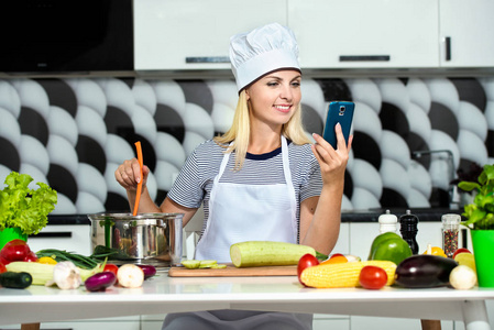 年轻女子在厨房做饭。 一个女孩正在手机上读食谱。健康的食物饮食。 健康的生活方式。 在家做饭。