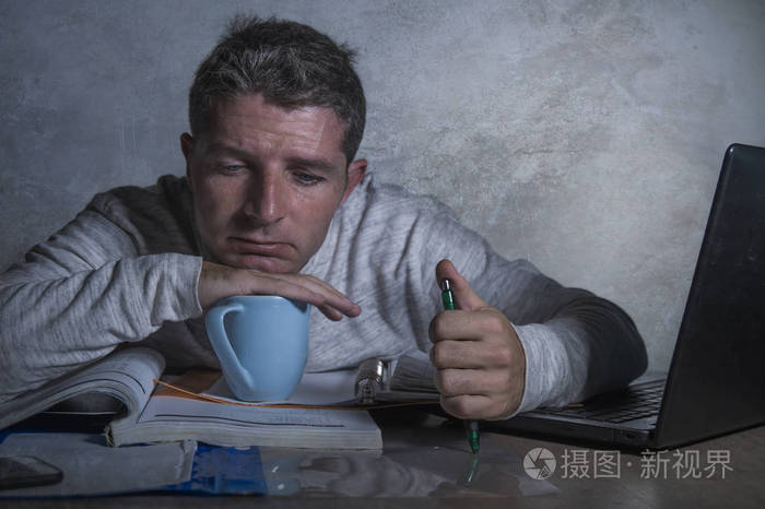 年轻的疲惫和困倦的男人在家里的办公桌上工作,手提电脑感到沮丧和