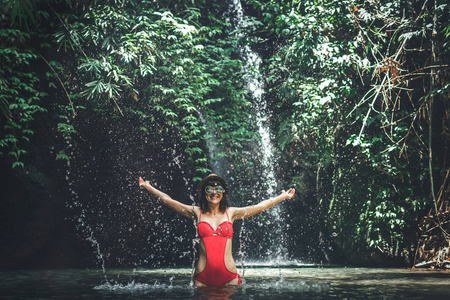 愉快的年轻妇女游客与草帽在深丛林与瀑布。真正的冒险概念。巴厘岛