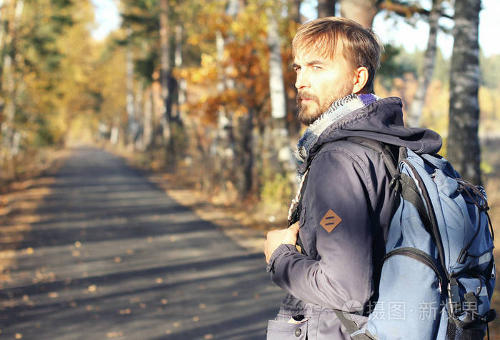 英俊的时髦男人带着背包在秋天的公园里散步. 发现美丽的秋天.