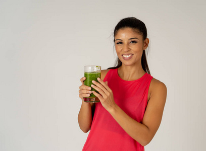 健身女性快乐微笑着拿着一杯绿色蔬菜冰沙健身后，在灰色背景下进行跑步锻炼，在美容健康健身饮食营养和健康生活方式的概念上。