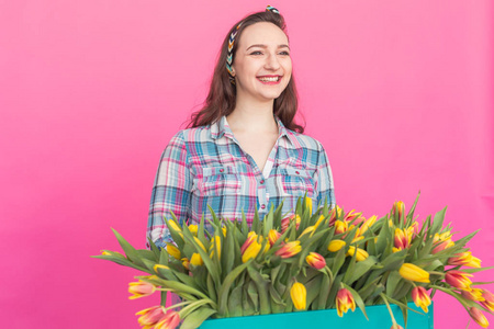 快乐的高加索年轻妇女与盒黄色郁金香粉红色背景