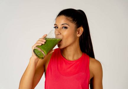 健身女性快乐微笑着拿着一杯绿色蔬菜冰沙健身后，在灰色背景下进行跑步锻炼，在美容健康健身饮食营养和健康生活方式的概念上。
