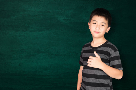 快乐的亚洲孩子微笑在空的绿色黑板与复制空间，以增加文字或文字教育，并回到学校的概念理念。