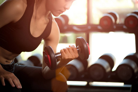 女子手握哑铃在健身房锻炼。 健身肌肉身体与一套黑色重量在健身房背景。 运动和健康的生活方式概念。