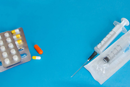 蓝色背景上的药片和注射器。 预防和治疗疾病