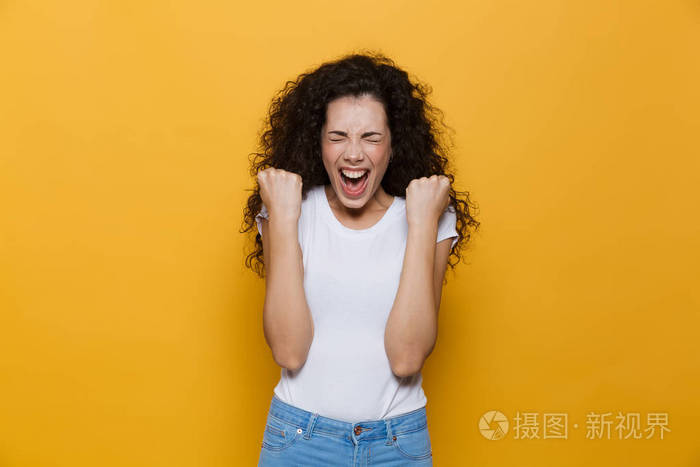 20多岁的快乐女人的画面她的卷发在黄色背景下尖叫着紧握着拳头