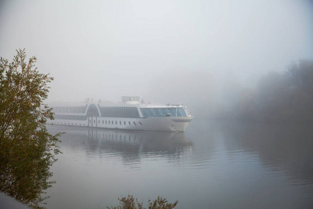 白大船在晨雾中漂浮在河上，秋景在蓝雾中