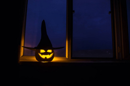 万圣节南瓜在神秘的房子窗户在晚上或万圣节南瓜在晚上的房间与蓝色的