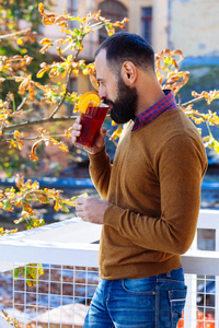 胡子男正坐在一家以秋叶为背景的咖啡馆里..穿着黄色毛衣的布鲁内特在咖啡馆或花园里喝酒，喝上温暖的覆盖葡萄酒。
