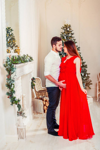 圣诞快乐的一对夫妇在壁炉边。 快乐的夫妇亲吻和拥抱。 由圣诞树装饰的客厅和礼物盒，灯光给人舒适的气氛。 在等孩子。 新年主题