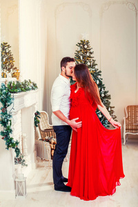 圣诞快乐的一对夫妇在壁炉边。 快乐的夫妇亲吻和拥抱。 由圣诞树装饰的客厅和礼物盒，灯光给人舒适的气氛。 在等孩子。 新年主题。 