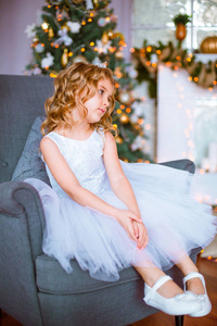 一个可爱的小女孩，家里有一头金发，靠近一棵圣诞树，里面有礼物花环和装饰的壁炉