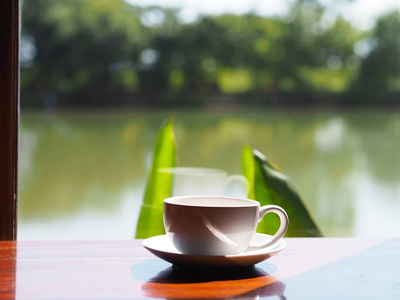 白色空杯咖啡放在玻璃窗旁边的木桌上，在热带花园的咖啡店里倒影。