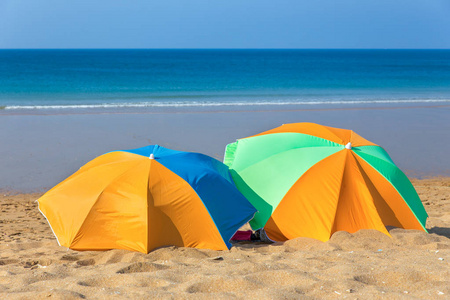海边沙滩上有两把五颜六色的沙滩伞