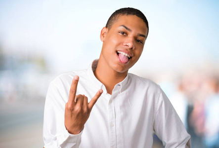 年轻的非裔美国人在镜头前露出舌头,滑稽的样子,在没有聚焦的户外背景