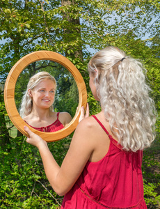 年轻的金发女人看着镜子的倒影图片