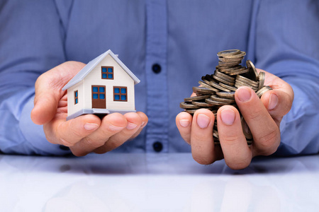 s Hand Holding House Model And Coins Over Desk