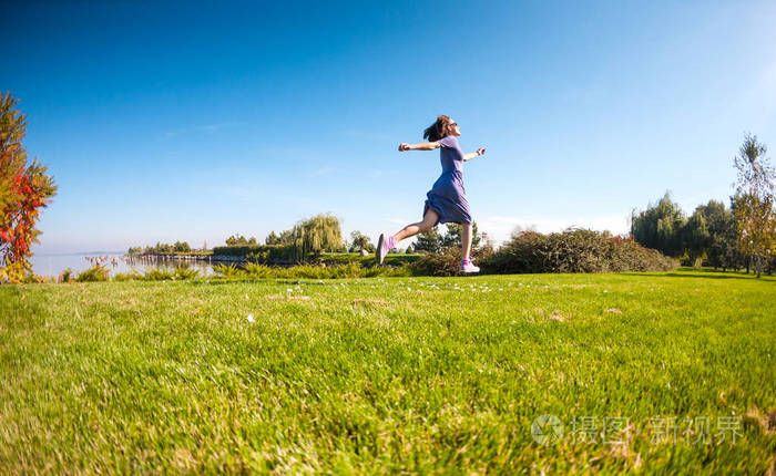 一个穿裙子的女孩穿过一片绿色的草地在公园里散步的女人自然界的活动