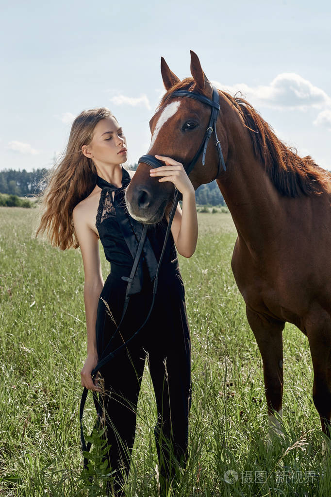女骑手站在田里的马旁边一个女人和母马的时尚肖像是草地上村庄里的马