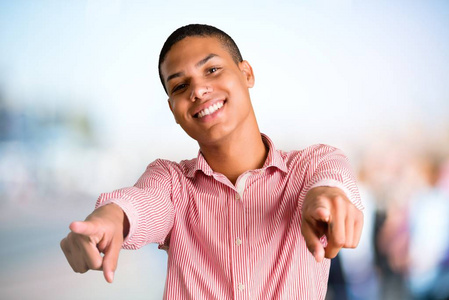 年轻的非裔美国人指着你,同时微笑着在没有重点的户外背景照片