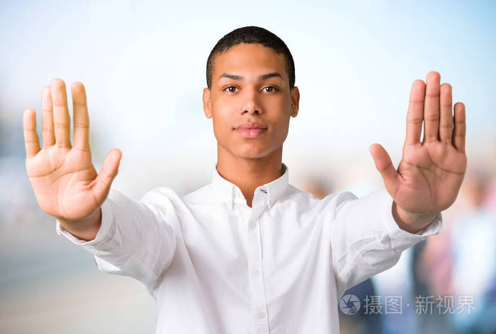 年轻的非裔美国男子用她的手做停止手势,因为对不集中的户外背景的