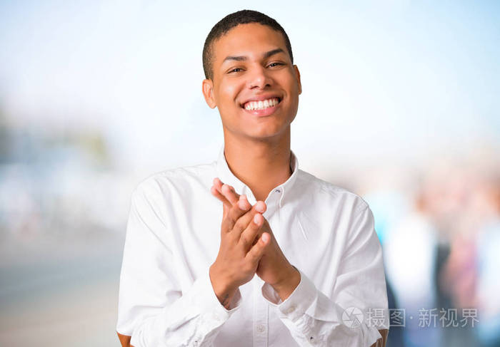 一位身穿白色衬衫的非裔美国年轻人在户外背景会议上发言后鼓掌