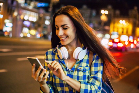 年轻的笑脸女人在明亮的城市街道上使用智能手机