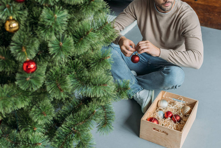 男人用装饰圣诞树，坐在家里的地板上
