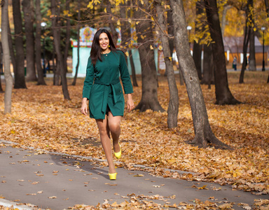 一位年轻美丽的黑发女子的肖像，穿着一件绿色的短外套，走在秋天的公园里
