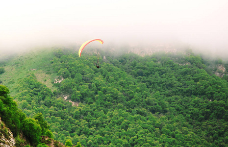 滑翔伞飞越美丽的山脉，覆盖着绿色的树林
