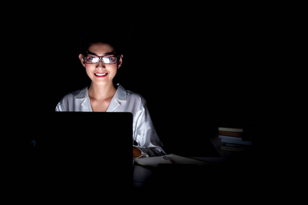 女人在她家的办公室工作到很晚。 美丽的亚洲女人在电脑上工作，戴着眼镜，开心地笑着。 现代全球连接的商业概念。