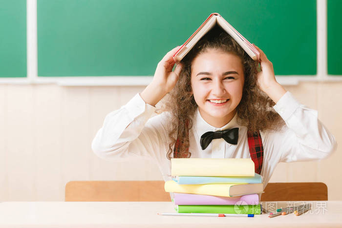 穿着校服的女学生坐在书桌前,桌上放着书和铅笔,背景是一块绿色的木板
