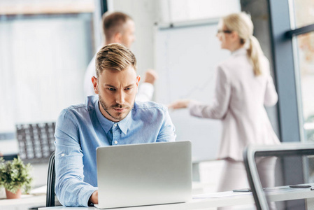 集中精力集中精力的年轻商人使用笔记本电脑和同事在办公室后面工作