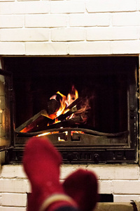 脚穿羊毛袜子在圣诞壁炉旁。 女人通过温暖的火来放松，穿着羊毛袜子热身她的脚。 站起来。 冬季和圣诞节假期的概念。