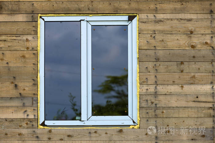 关闭新的窄塑料乙烯基窗的细节安装在棕色天然木板和木板的房子墙上房