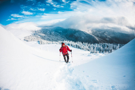 一个穿着雪鞋和在山上徒步旅行的人。 冬季旅行。 攀登攀登者在美丽的天空与云。 积极的生活方式。 在雪地里爬山。