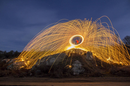 长曝光镜头的人站在岩石山旋转钢毛圈,使烟花的亮黄色发光火花在蓝色