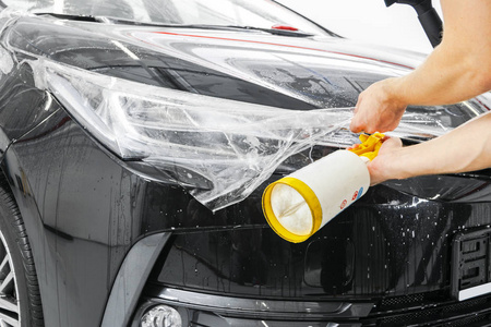汽车包装专家把乙烯基箔或薄膜放在汽车上。 保护膜。 使用带有工具的保护膜进行工作。 汽车细节。 透明薄膜。 汽车油漆保护。 修剪