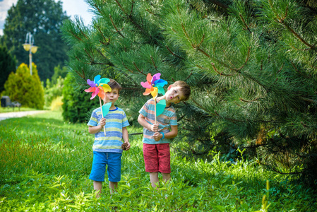 两个快乐的孩子在花园里玩风车手轮。 可爱的兄弟姐妹是最好的朋友。 可爱的男孩微笑春天或夏天公园。 户外休闲友谊家庭概念。