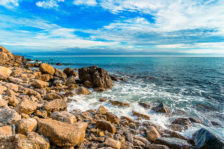 黑海的石质海岸拍打着克里米亚俄罗斯。 不同大小的黄色石头，远处有白色的泡沫海，蓝天有云